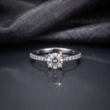 Silver CZ Solitaire Pavé Shoulder Engagement Ring front top view on dark grey mirror surface with grey fabric backdrop showing round brilliant CZ solitaire centre stone in 4-claw rhodium prong setting with single-row micro-pave CZ shoulder stones on slim tapered band with sparkle starburst effect and mirror reflection below