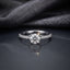 Silver CZ Solitaire Pavé Shoulder Engagement Ring front top view on dark grey mirror surface with grey fabric backdrop showing round brilliant CZ solitaire centre stone in 4-claw rhodium prong setting with single-row micro-pave CZ shoulder stones on slim tapered band with sparkle starburst effect and mirror reflection below
