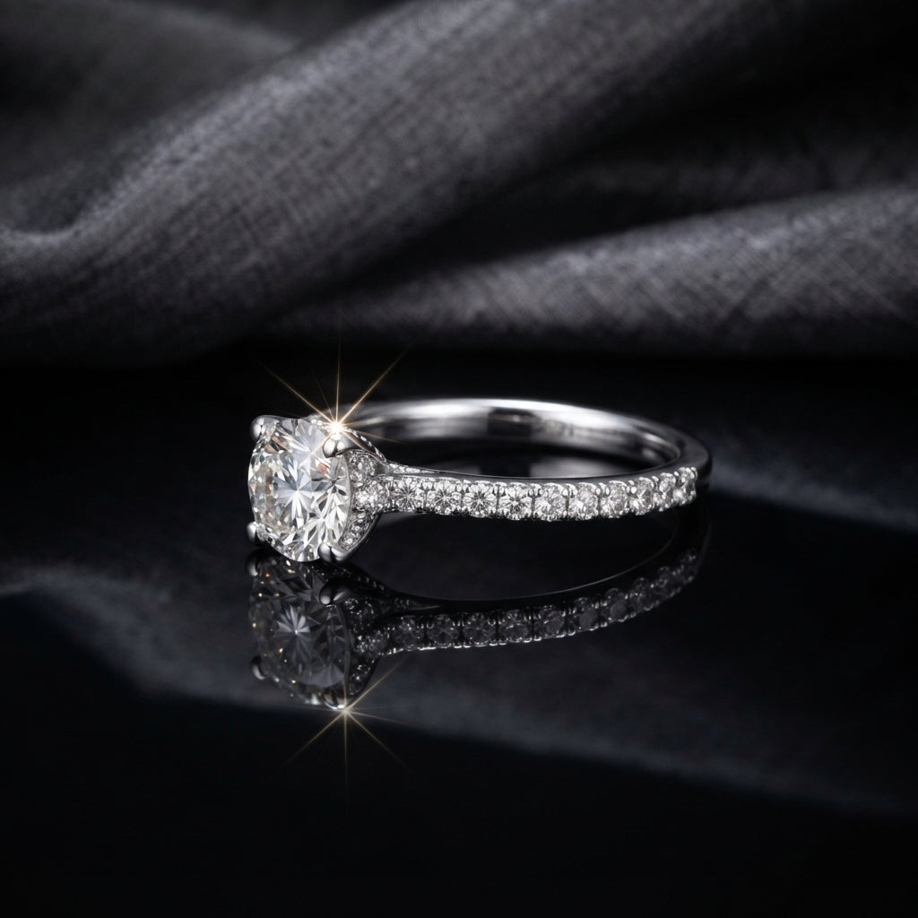 Silver CZ Solitaire Pavé Shoulder Engagement Ring side profile view on black mirror surface with dark grey fabric backdrop showing round brilliant CZ solitaire in 4-claw rhodium prong setting on slim tapered shank with single-row micro-pave CZ shoulder stones with sparkle starburst effect and mirror reflection below