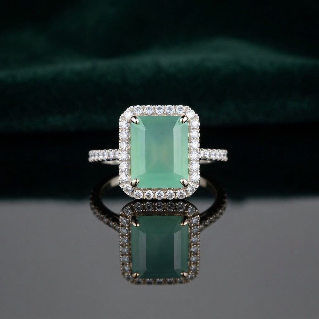 Silver Emerald Cut CZ Rectangular Halo Pave Band Solitaire Ring in Sapphire Blue variant on dark mirror surface with dark teal velvet backdrop showing deep royal sapphire blue emerald-cut CZ solitaire in 4-claw setting with full rectangular white CZ halo and continuous micro-pave white CZ band in rhodium silver with mirror reflection below
