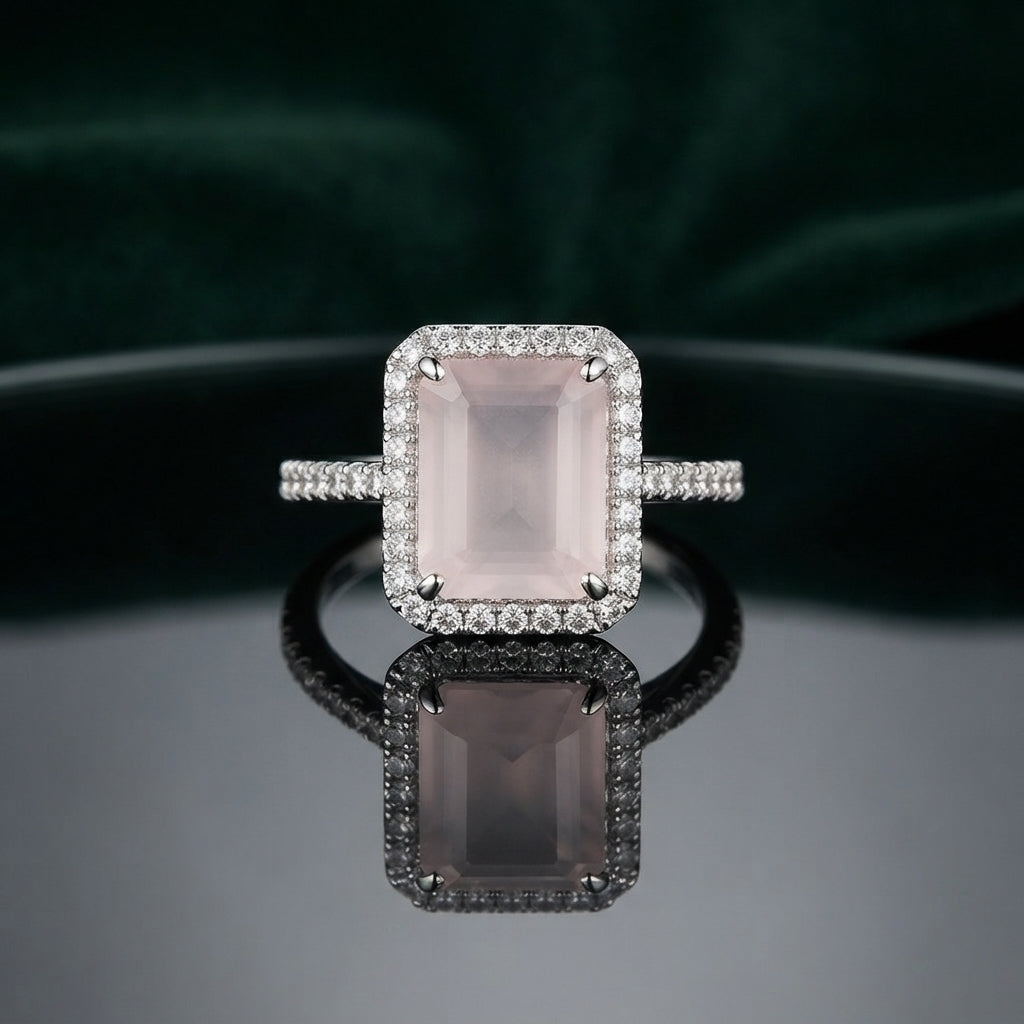 Silver Emerald Cut CZ Rectangular Halo Pave Band Solitaire Ring in Rose Pink Morganite variant on dark mirror surface with dark teal velvet backdrop showing soft blush rose pink emerald-cut CZ solitaire in 4-claw setting with full rectangular white CZ halo and continuous micro-pave white CZ band in rhodium silver with mirror reflection below