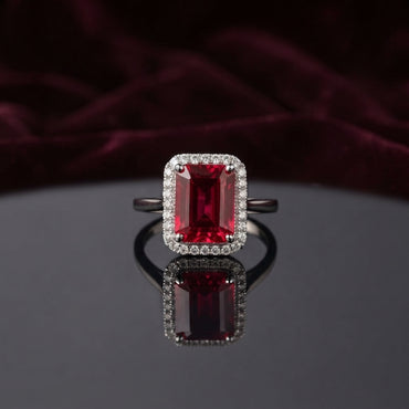 Silver Emerald Cut CZ Rectangular Halo Pave Band Solitaire Ring in Diamond White Clear CZ variant on dark mirror surface with charcoal satin backdrop showing brilliant clear diamond-illusion emerald-cut CZ solitaire in 4-claw setting with full rectangular white CZ halo and continuous micro-pave white CZ band in rhodium silver with mirror reflection below