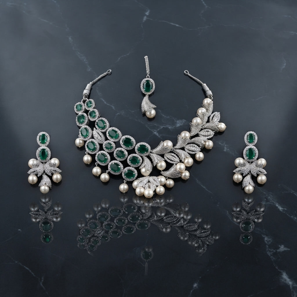 Silver Emerald CZ Halo Pearl Drop Leaf Bib Necklace Earrings & Maang Tikka Bridal Set on dark grey marble surface with teal velvet drape backdrop