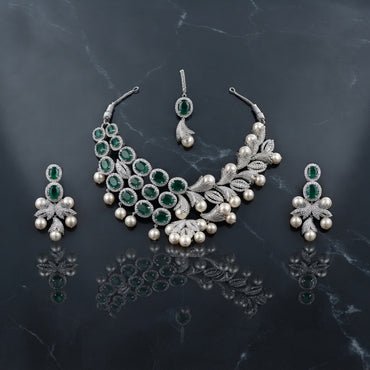 Silver Emerald CZ Halo Pearl Drop Leaf Bib Necklace Earrings & Maang Tikka Bridal Set on dark grey marble surface with teal velvet drape backdrop