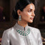 Silver Emerald Green CZ 3-Layer Emerald-Cut Tennis Necklace and Earrings Luxury Bridal Set worn by South Asian model in silver grey silk kurta with embroidered neckline in luxury jewelry store setting showing triple-strand layered collar necklace and long 3-stone drop earrings with emerald green CZ stones