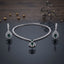 Silver Emerald Green CZ Floral Scroll Pendant Necklace and Earrings 2-Piece Set on dark grey mirror surface with dark wood backdrop gold pearls and dried botanicals showing double-row CZ tennis necklace with open baroque scroll floral pendant and large emerald green pear CZ centre flanked by matching long chandelier drop earrings with CZ leaf spray top and emerald green pear CZ centre with mirror reflections below