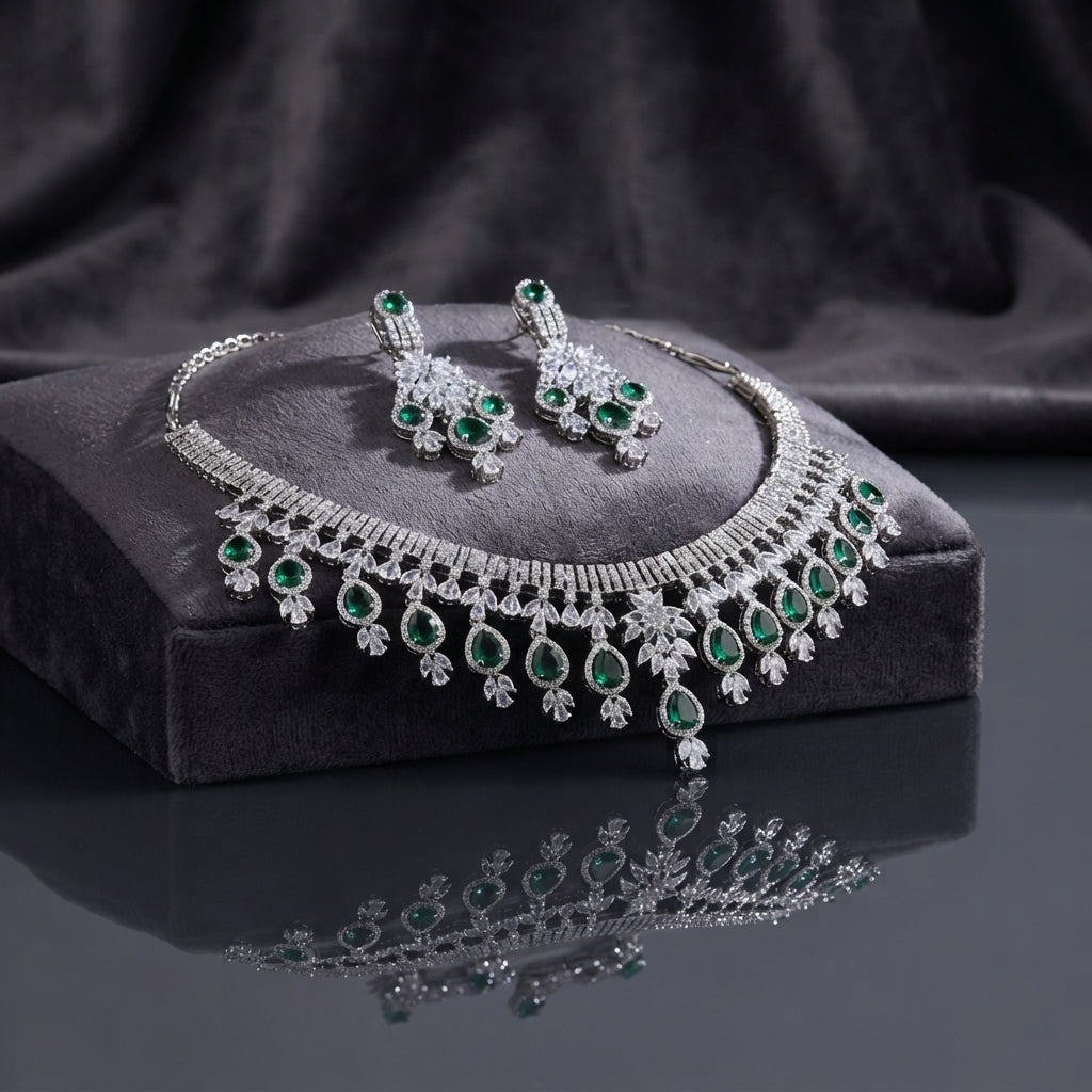 Silver Emerald Green CZ Fringe Tassel Bridal Necklace and Earrings 2-Piece Luxury Set on dark charcoal stone display block with dark grey silk backdrop showing grand V-fringe statement necklace with double-row baguette CZ top bar and graduated emerald green pear CZ tassel drops with matching chandelier drop earrings featuring emerald green CZ cluster and teardrop drops with mirror reflection below