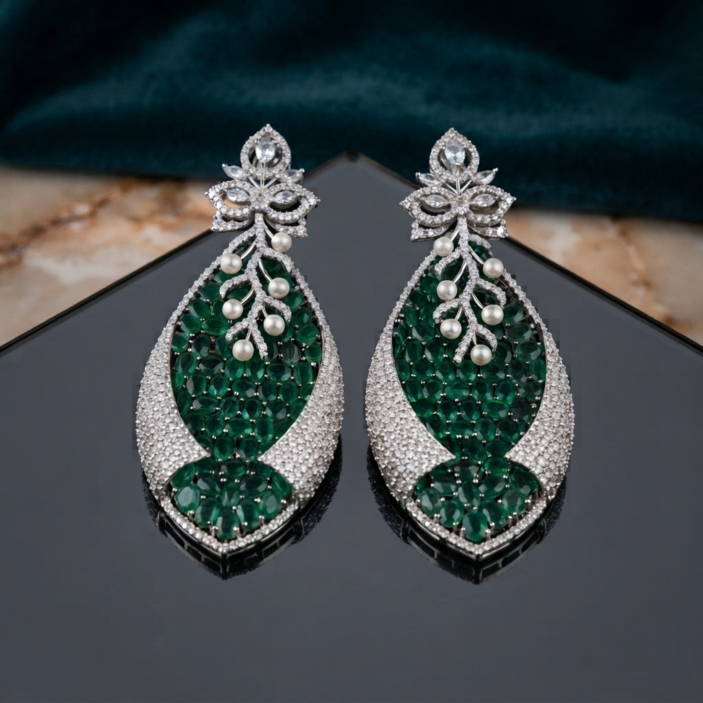 Silver Emerald Green CZ Oval Cluster and Pearl Vine Twisted Leaf Grand Drop Earrings flat lay on dark mirror surface with teal velvet backdrop showing pair detail with reflection of white CZ lotus stud and dense oval emerald CZ twisted leaf drop with pearl vine overlay and stepped CZ base