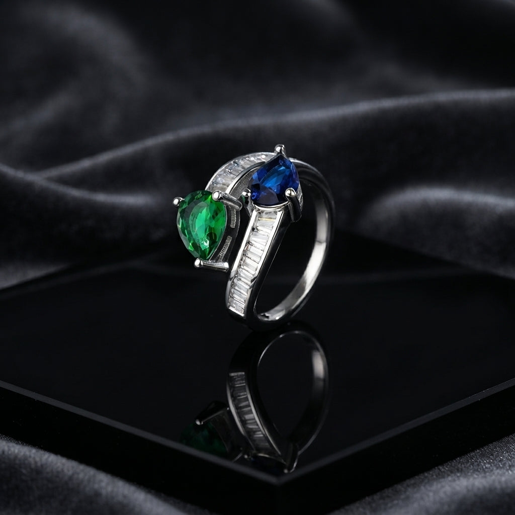 Silver Emerald Green & Royal Sapphire Blue Toi et Moi Pear CZ Baguette Bypass Cocktail Ring on black lacquer tray with dark grey satin drape backdrop
