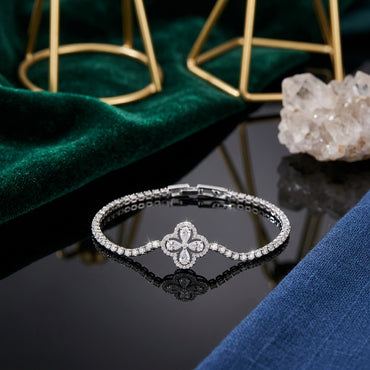 Silver-Tone Four-Petal Clover Pear CZ Floral Centerpiece Pavé Tennis Bracelet on black reflective surface with emerald green velvet fabric, gold geometric display stand and white quartz crystal cluster backdrop