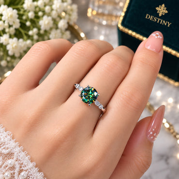 Silver-Tone Large Round Brilliant Emerald Green CZ 4-Prong Solitaire Marquise Accent Pavé Shoulder Delicate Band Ring worn on model hand with bridal lace outfit, white flowers and Destiny jewelry box in background