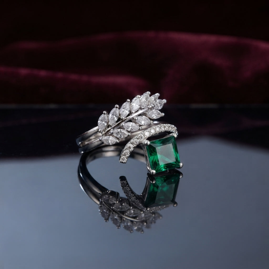 Silver Marquise Leaf Crown Princess CZ Adjustable Cocktail Ring in Emerald Green — rhodium-plated open adjustable ring with marquise white CZ leaf crown, micro-pavé arc, and deep emerald green princess cut center stone, on dark mirror with burgundy velvet backdrop