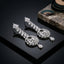 Silver-Tone Marquise Pear CZ Cluster Top Double Baguette Waterfall Column & Baguette Sunburst Fan Medallion Pear Drop Chandelier Earrings on black mirror surface with marble stone prop and teal green silk fan backdrop