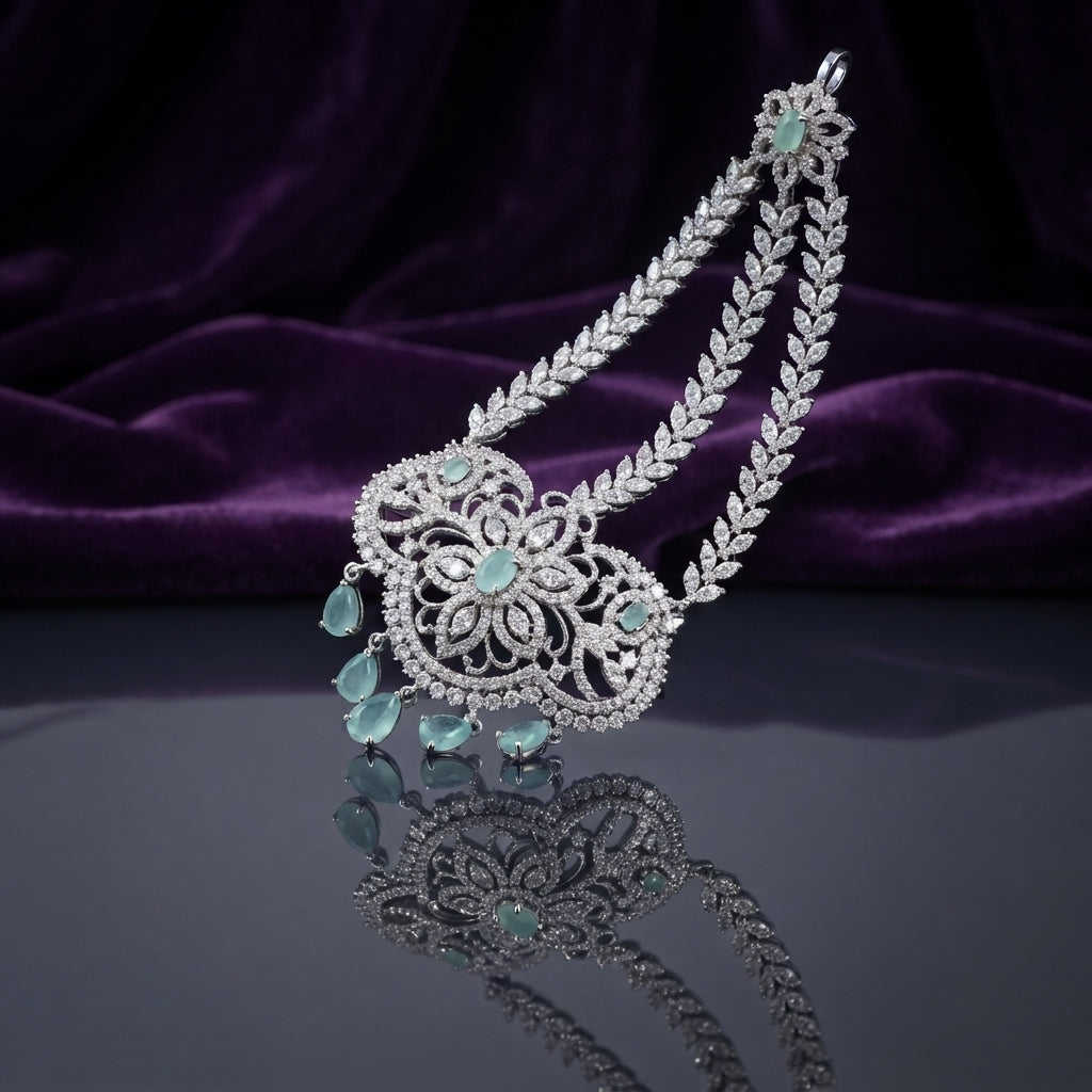 Silver Mint Green CZ Floral Filigree and Marquise Wheat Chain Grand Maang Tikka on dark mirror surface with purple velvet backdrop showing rhodium silver double-strand marquise white CZ wheat chain with 3-medallion open filigree flower pendant mint green CZ cabochon centres and 5 mint green pear drop fringe