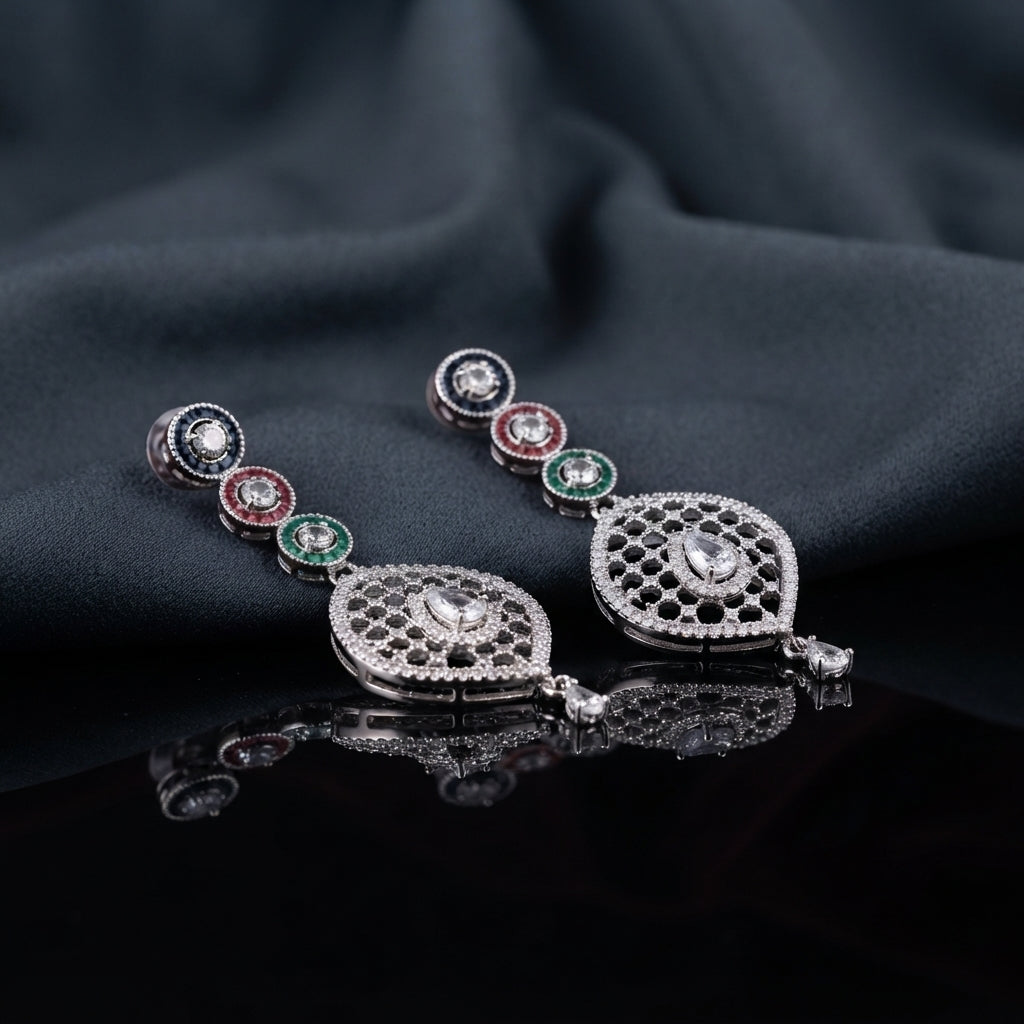 Silver Multi-Color CZ Circle Chain and Open Oval Filigree Pear Drop Earrings — rhodium silver-tone bridal earrings with 3-tier sapphire blue ruby red and emerald green baguette CZ circle disc chain open black rhodium oval honeycomb filigree pendant with large pear white CZ center and pear CZ tip drop displayed on dark black mirror surface with charcoal satin backdrop