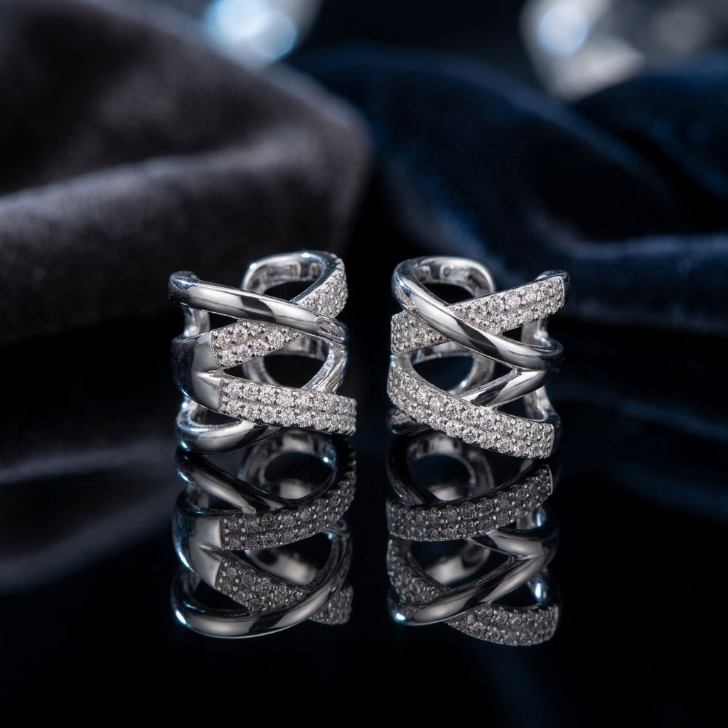 Silver-Tone Multi-Row Crossover Pavé White CZ Huggie Hoop Ear Cuff Earrings pair on black reflective surface with navy blue velvet fabric backdrop