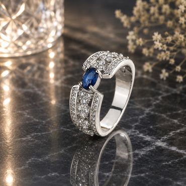 Silver-Tone Oval Blue Sapphire CZ Art Deco Pavé Panel Wide Band Ring on dark black marble surface with crystal bokeh light orb and white baby's breath flowers backdrop