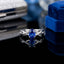 Silver-Tone Oval Blue Sapphire CZ Halo & Infinity Crossover Pavé Band Ring on black reflective surface with royal blue velvet ring box and silver glitter clutch backdrop