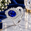Silver-Tone Oval Royal Sapphire Blue CZ Micro-Pavé Inner Halo & Baguette Sunburst Outer Halo Adjustable Cocktail Ring on white marble surface with blue velvet fabric, white flowers and crystal geometric candleholder