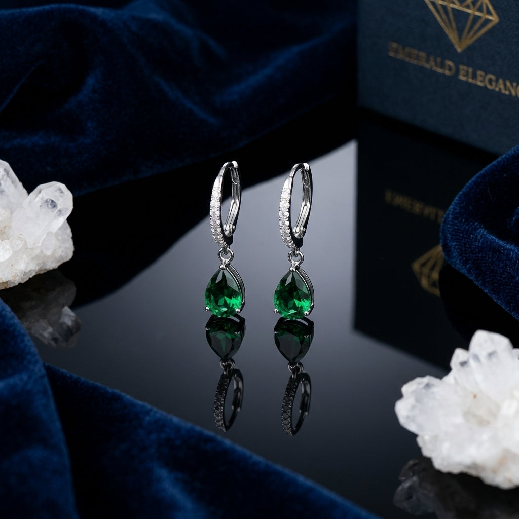 Silver-Tone Pavé CZ Huggie Hoop & Pear Emerald Green CZ Solitaire Drop Earrings pair on black reflective surface with navy blue velvet fabric and white quartz crystal clusters backdrop