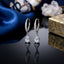 Silver-Tone Pavé CZ Huggie Hoop & Pear White CZ Solitaire Drop Earrings pair on black reflective surface with navy blue silk fabric and white quartz crystal cluster backdrop