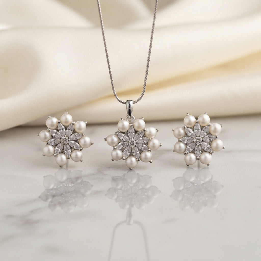 Silver Pearl CZ Daisy Flower Pendant Necklace Earrings Set on white marble surface with cream silk fabric backdrop showing rhodium silver-tone snake chain pendant necklace and matching pair of stud earrings each featuring snowflake daisy flower cluster with marquise-cut white CZ star petal arrangement and outer ring of round faux pearl cabochons with mirror reflection below