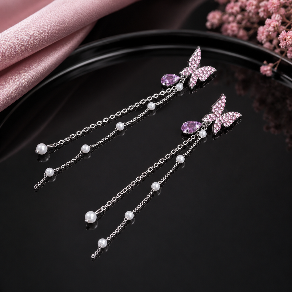 Silver-Tone Pink CZ Micro-Pavé Butterfly & Amethyst Purple Pear CZ Drop Pearl Station Long Chain Tassel Earrings on black round tray with pink satin fabric and dried pink flowers in background
