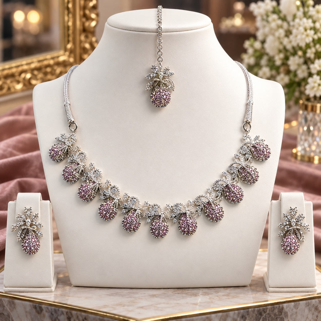 Silver Pink CZ Teardrop Cluster and White CZ Bow Floral Necklace Earrings Set worn by model in dusty pink mauve net lehenga showing 7-drop graduating collar necklace with pink CZ micro-pavé teardrop bodies and white CZ bow connectors with matching drop earrings in warm bokeh editorial setting