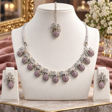 Silver Pink CZ Teardrop Cluster and White CZ Bow Floral Necklace Earrings Set worn by model in dusty pink mauve net lehenga showing 7-drop graduating collar necklace with pink CZ micro-pavé teardrop bodies and white CZ bow connectors with matching drop earrings in warm bokeh editorial setting
