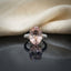 Silver Rose Gold Oval Morganite CZ Solitaire Bridal Ring top view on dark grey mirror surface with ivory cream silk backdrop showing large oval peach-pink morganite CZ solitaire centre stone in 4-claw rose gold prong setting with triple-row micro-pave white CZ shoulders on split shank band with mirror reflection below