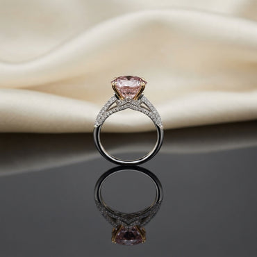 Silver Rose Gold Oval Morganite CZ Solitaire Bridal Ring side profile view on dark grey mirror surface with ivory cream silk backdrop showing large oval peach-pink morganite CZ solitaire in 4-claw rose gold prong setting on two-tone split shank band with triple-row micro-pave white CZ shoulders and V-shaped chevron accent with mirror reflection below