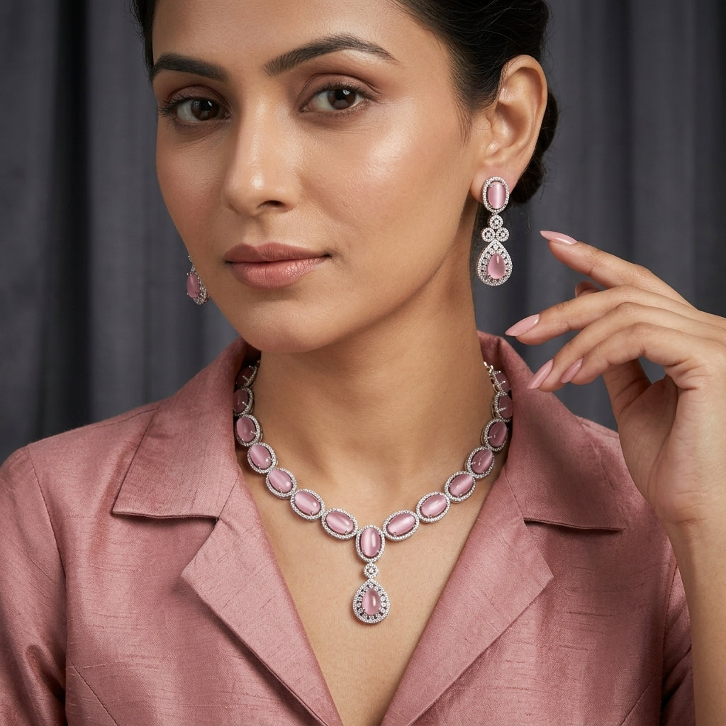Silver Rose Pink Moonstone CZ Halo Oval Tennis Necklace and Drop Earrings Set — South Asian model wearing rhodium-plated silver-tone graduated oval rose pink moonstone cabochon tennis necklace with pear drop pendant and matching 3-tier moonstone halo drop earrings, styled with dusty rose silk blazer against dark grey backdrop