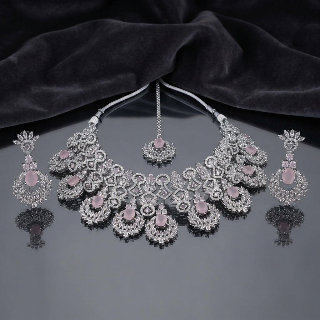 Silver Rose Quartz CZ Grand Mughal Bib Necklace Maang Tikka and Cascade Drop Earrings Bridal Set — rhodium silver-tone 3-piece grand bridal set with 5-unit Mughal arch bib necklace featuring oval rose quartz CZ cabochons white CZ micro-pavé scrollwork and radiating marquise CZ leaf crown borders matching maang tikka with rose quartz CZ floral crown and 4-tier cascade drop earrings displayed on dark grey mirror surface with black satin backdrop