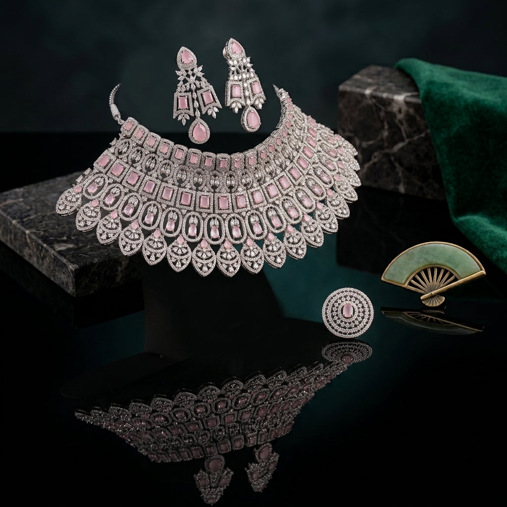 Silver-Tone Rose Quartz Pink Cushion Oval CZ Pavé Wide Tiered Mughal Bib Choker Necklace Chandelier Earrings Maang Tikka & Ring 4-Piece Bridal Set styled on dark stone surface with green velvet drape and jade fan backdrop