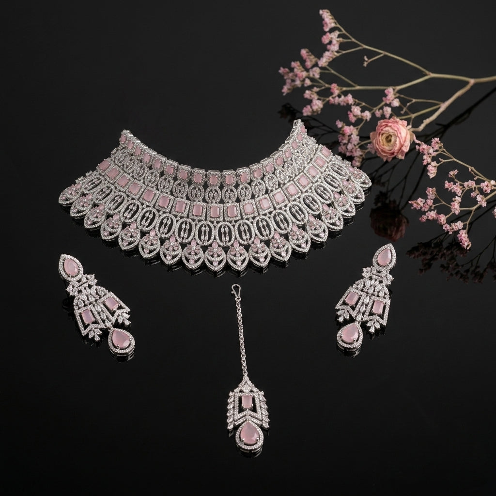 Silver-Tone Rose Quartz Pink Cushion Oval CZ Pavé Wide Tiered Mughal Bib Choker Necklace Chandelier Earrings Maang Tikka & Ring 4-Piece Bridal Set on black mirror surface with pink ranunculus flowers and pink baby's breath floral backdrop