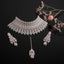 Silver-Tone Rose Quartz Pink Cushion Oval CZ Pavé Wide Tiered Mughal Bib Choker Necklace Chandelier Earrings Maang Tikka & Ring 4-Piece Bridal Set on black mirror surface with pink ranunculus flowers and pink baby's breath floral backdrop