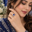 Silver Round CZ Sunflower Halo Milgrain Infinity Shoulder Cocktail Ring in Sapphire Blue variant worn on finger of Pakistani female model in navy blue embroidered outfit in luxury backdrop with white flowers showing large sapphire blue round CZ solitaire with full white CZ sunflower halo and open infinity milgrain shoulders in rhodium silver