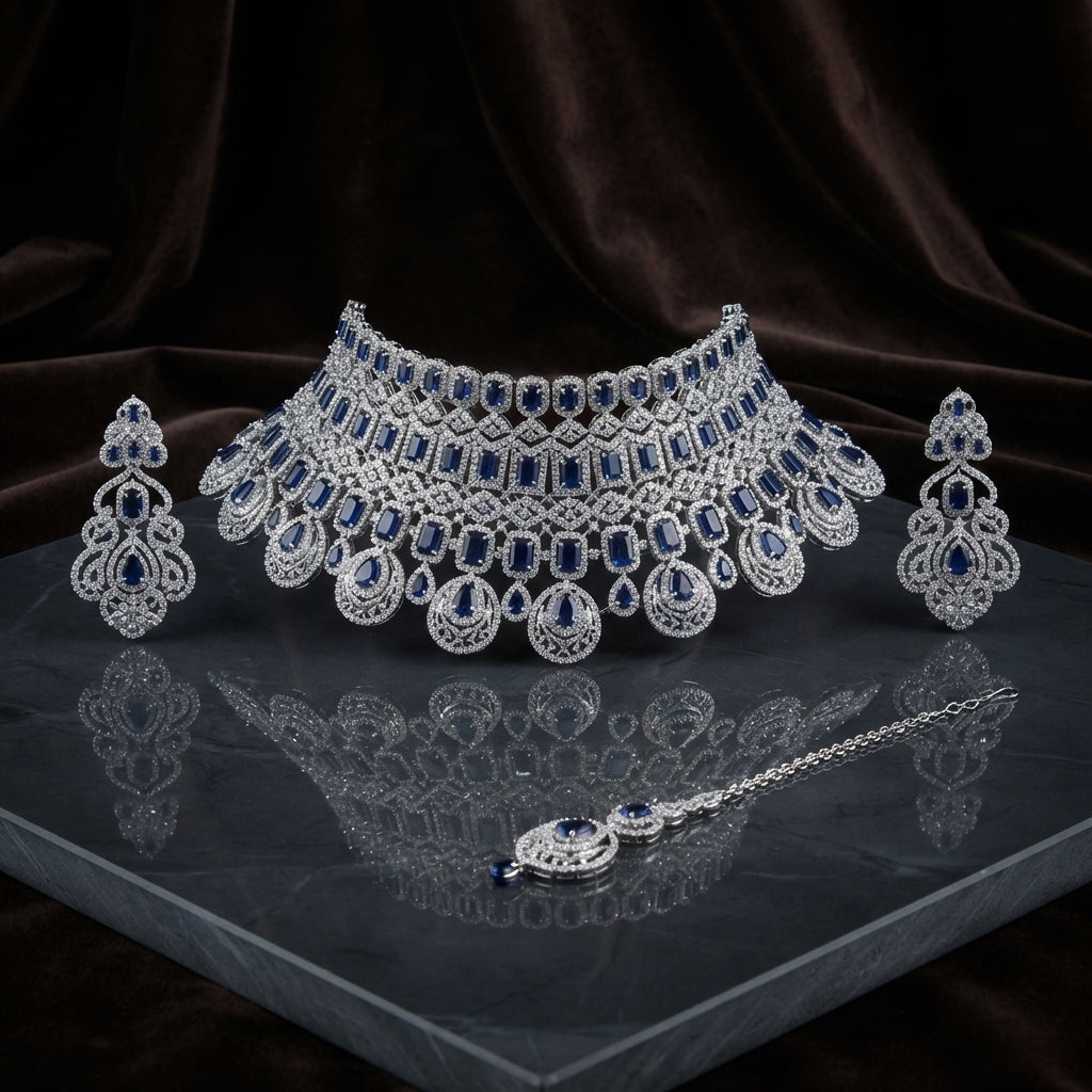 Silver Royal Blue Sapphire CZ Grand Bib Choker Drop Earrings & Maang Tikka Grand Bridal Set on dark grey mirror surface with dark brown velvet drape backdrop