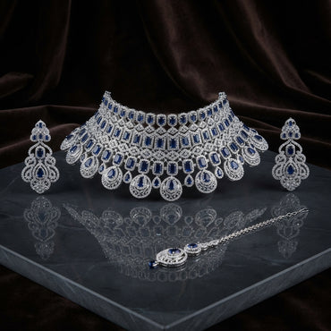 Silver Royal Blue Sapphire CZ Grand Bib Choker Drop Earrings & Maang Tikka Grand Bridal Set on dark grey mirror surface with dark brown velvet drape backdrop
