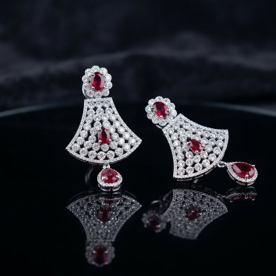 Silver Ruby CZ Floral Fan and Pear Halo Drop Earrings — rhodium silver-tone statement bridal earrings with ruby CZ oval daisy floral stud wide fan body in dense interlocking white CZ cluster honeycomb with ruby CZ center oval and large ruby CZ pear halo drop displayed on dark black mirror surface with charcoal satin backdrop