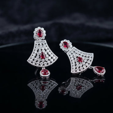 Silver Ruby CZ Floral Fan and Pear Halo Drop Earrings — rhodium silver-tone statement bridal earrings with ruby CZ oval daisy floral stud wide fan body in dense interlocking white CZ cluster honeycomb with ruby CZ center oval and large ruby CZ pear halo drop displayed on dark black mirror surface with charcoal satin backdrop