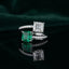 Silver Toi et Moi Dual Cushion CZ Bypass Ring in White and Emerald Green CZ variant flat lay on dark mirror surface with deep green satin backdrop showing open bypass ring with full white CZ micro-pave shank and two large cushion cut CZ solitaires one clear white Asscher cut and one deep emerald green with mirror reflection