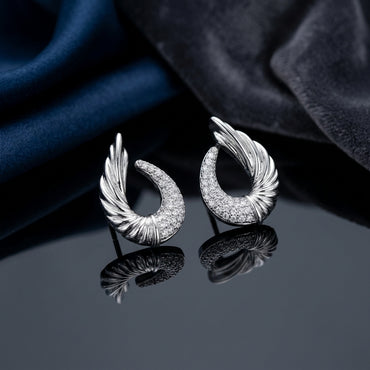 Silver-Tone Angel Wing Feather Crescent Pavé White CZ Stud Earrings pair on dark reflective surface with deep navy blue silk fabric backdrop