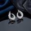 Silver-Tone Angel Wing Feather Crescent Pavé White CZ Stud Earrings pair on dark reflective surface with deep navy blue silk fabric backdrop