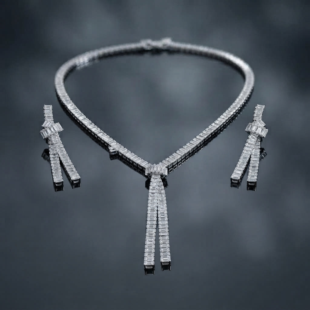 Silver-Tone Baguette CZ Tennis Collar and Triple Tassel Drop Earrings Set flat lay on dark grey mirror surface showing single-row channel-set baguette CZ tennis collar necklace with V-dip center knot and three slim baguette CZ tassel fringe drops beside matching pair of triple tassel drop earrings with baguette CZ knot stud top with mirror reflections below