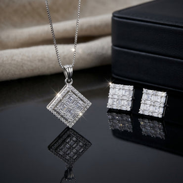 Silver-Tone Baguette and Round CZ Multi-Row Diamond Pendant and Earrings Set flat lay on dark black mirror surface with beige linen and black jewelry box backdrop showing large rhombus diamond pendant with baguette CZ grid center and round micro-pave CZ halo on silver box chain with ridged bail beside matching square stud earrings with baguette CZ grid and round CZ corners with mirror reflections below
