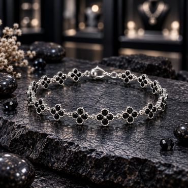 Silver-tone linked bracelet with black four-petal clover motifs, bead-like petal borders, small round centres and a lobster-style clasp, arranged on dark slate.