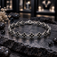 Silver-tone linked bracelet with black four-petal clover motifs, bead-like petal borders, small round centres and a lobster-style clasp, arranged on dark slate.