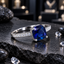 Silver-tone ring with a faceted cushion-shaped blue centre in a four-prong setting and rows of small round clear accents on the band shoulders.