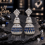 Pair of silver-tone tiered AD jhumka earrings with clear crown-like tops, sparkling upper bells and navy blue teardrop rows on the lower domes.